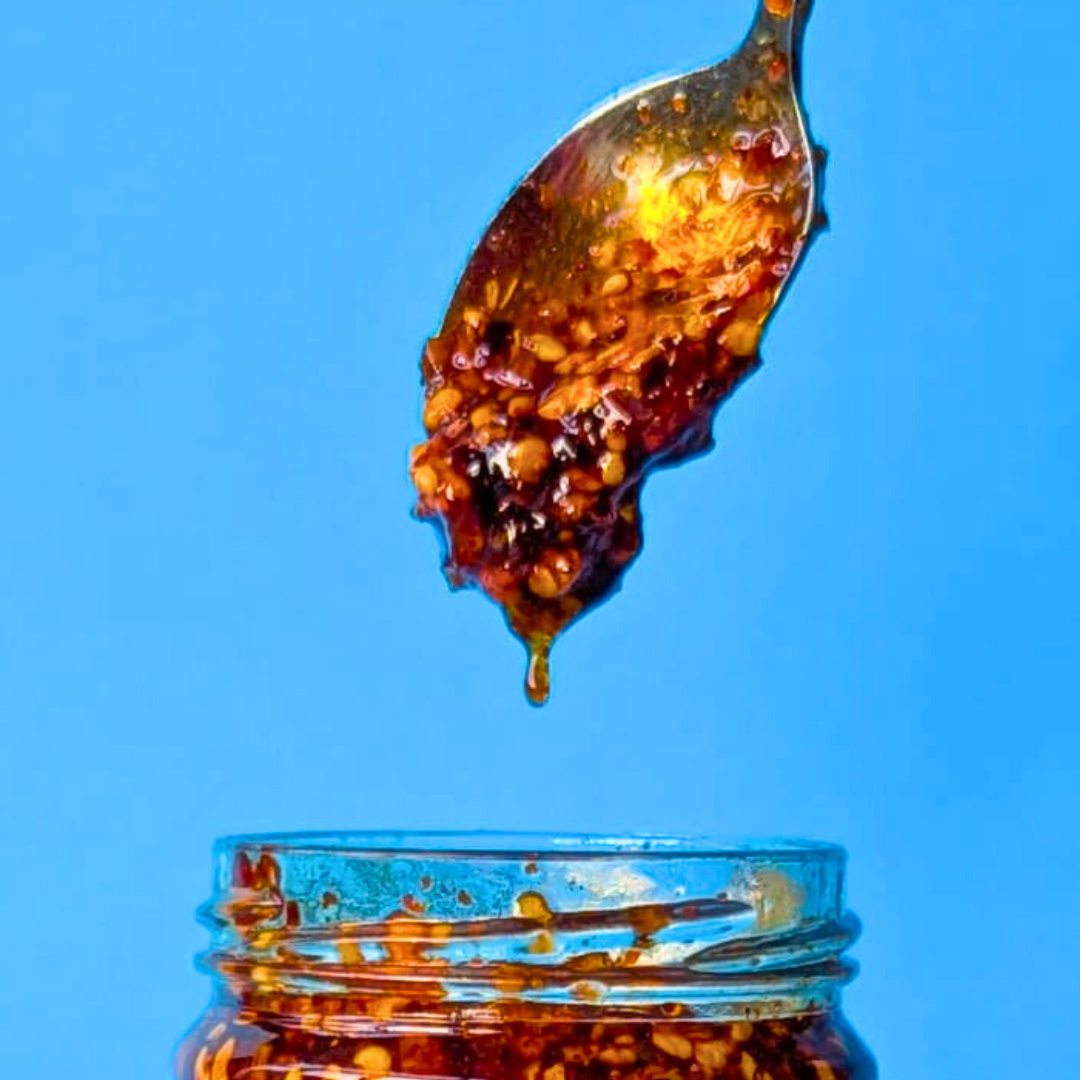 A close-up of a spoonful of crispy chilli oil (chili olie) dripping back into a glass jar.