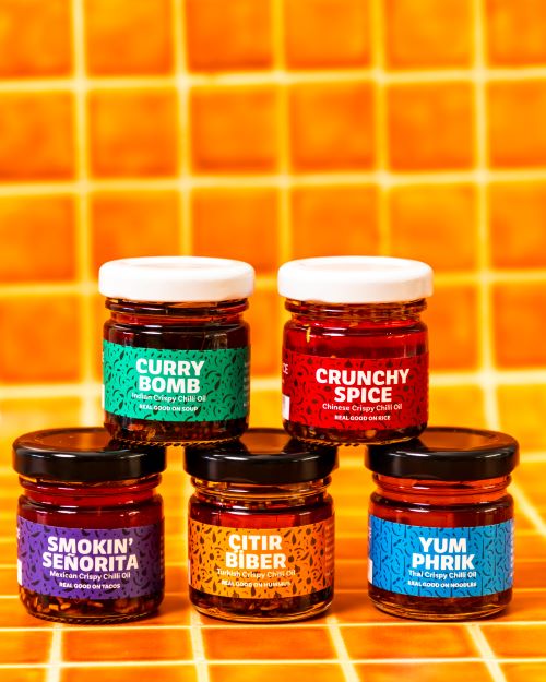 Trouble & Spice crispy chilli oil – chili olie  gift pack featuring five colorful jars, displayed in front of vibrant orange tiles. Perfect for kerst gift and corporate gifting.