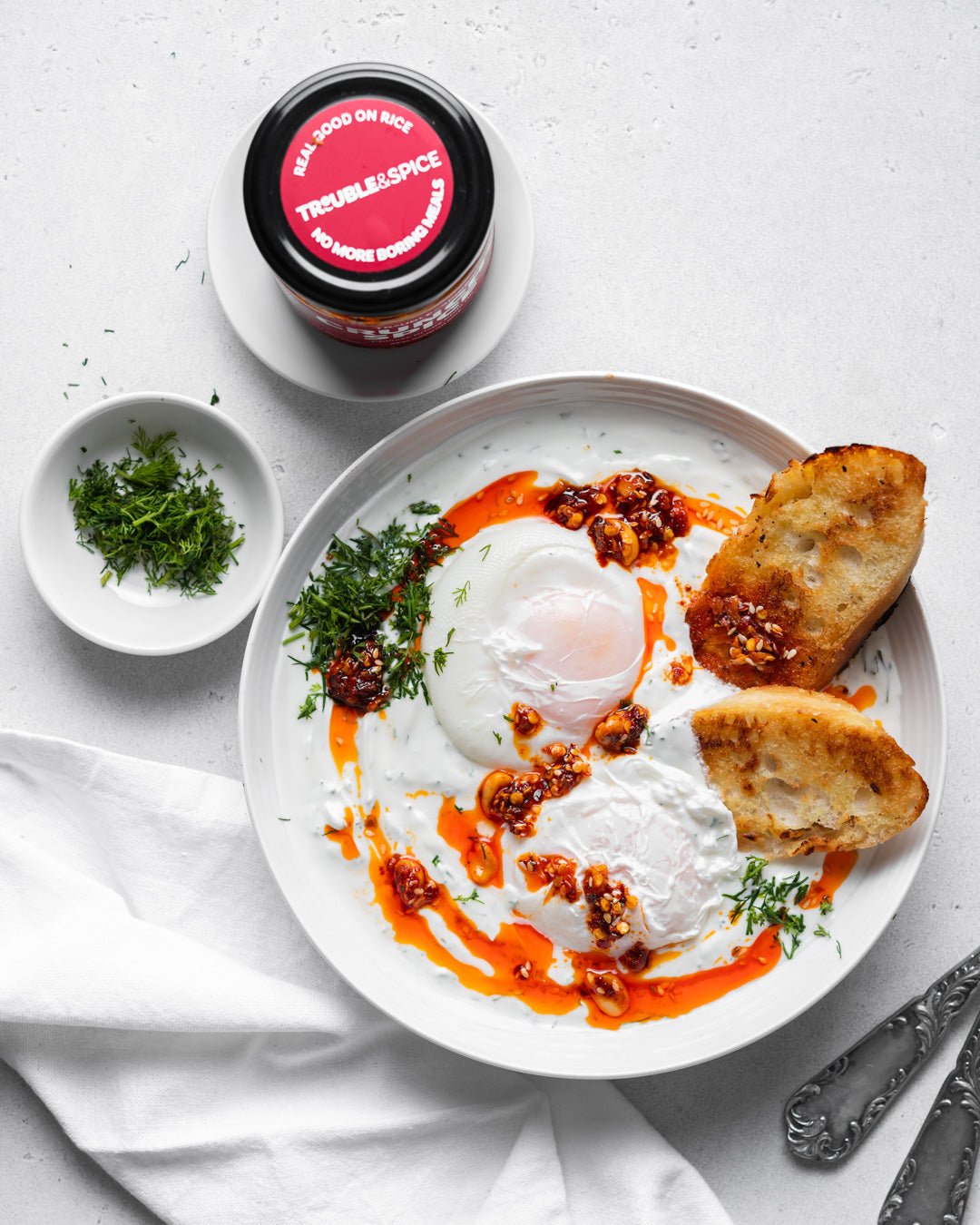 Poached eggs with yoghurt, crispy sourdough, and Trouble and Spice Crunchy Spice crispy chilli oil - chili olie– a bold, flavour-packed breakfast.