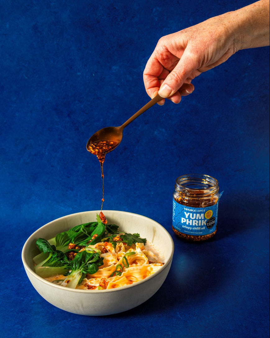 Hand pouring sauce from a jar over a bowl of food on a blue background