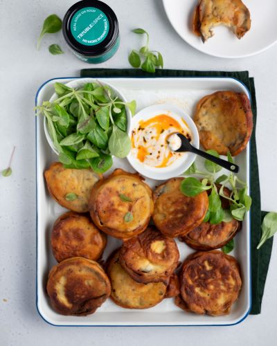 Golden aubergine fritters served with greens and a chilli oil - chile olie yogurt dipping sauce, featuring Trouble & Spice green-labeled jar.